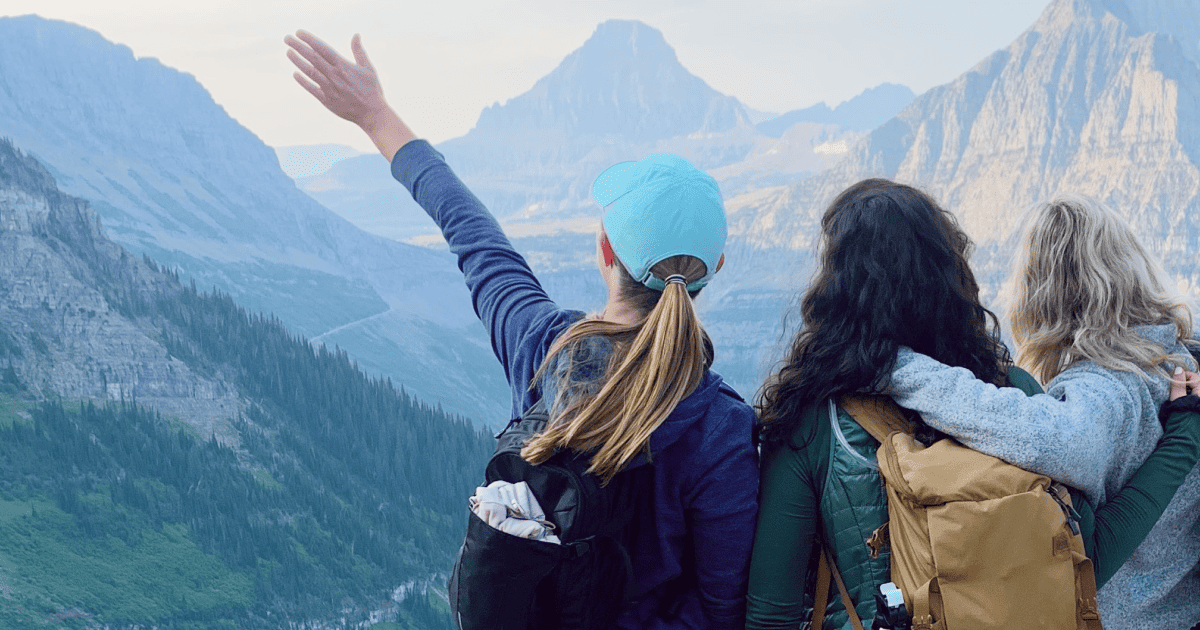 Three female friends with their arms around each other looking towards the mountains with open arms