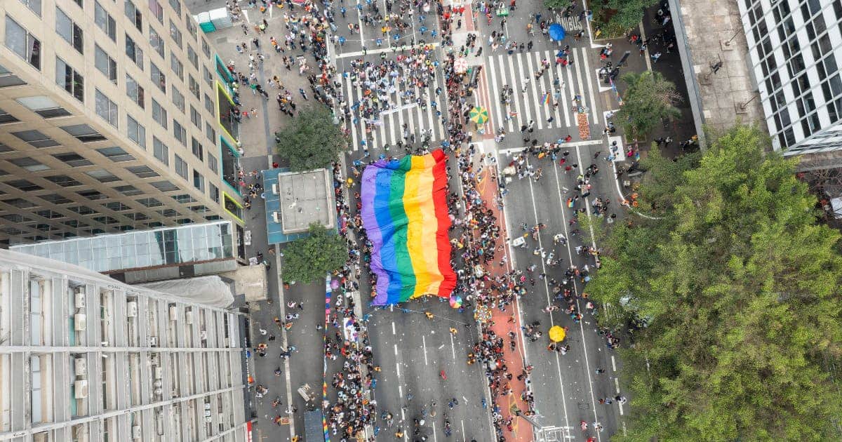 Overhead picture of the pride parade going down the street in São Paulo, Brazil with people holding up a rainbow flag.