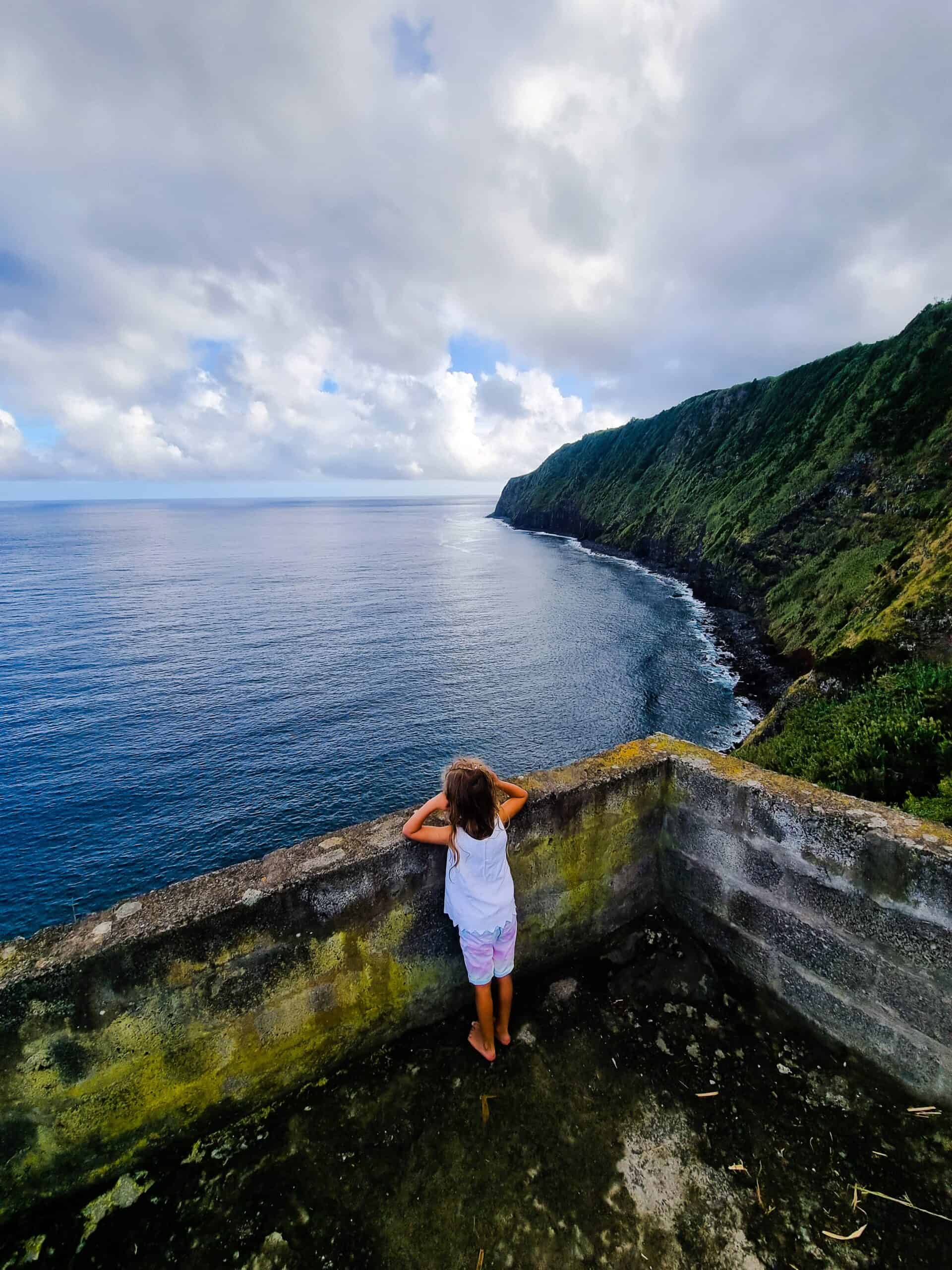 A little girl staring at the sea over a cement wall