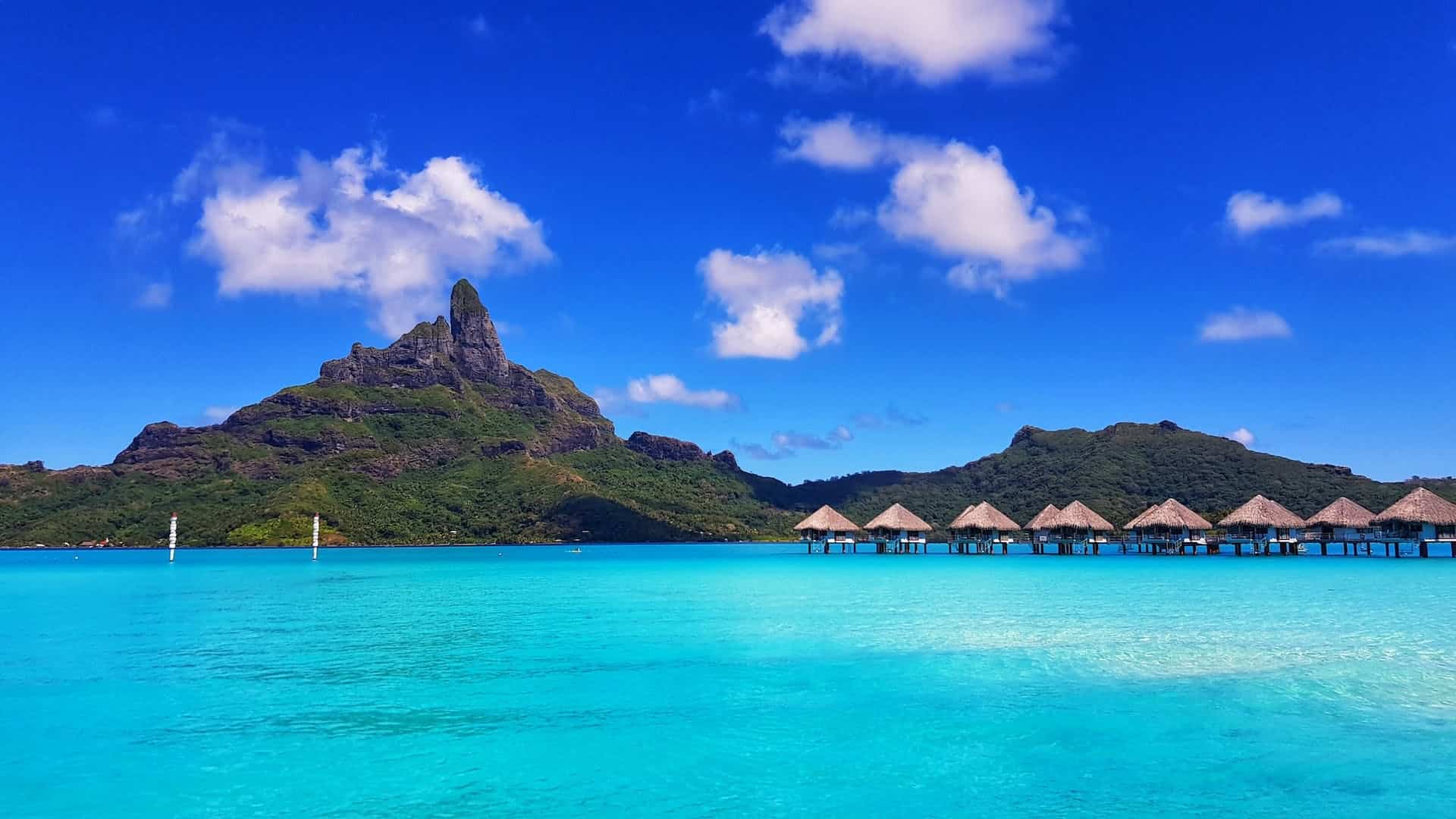 Huts in the water in Bora Bora surrounded by the ocean with mountains in the background.