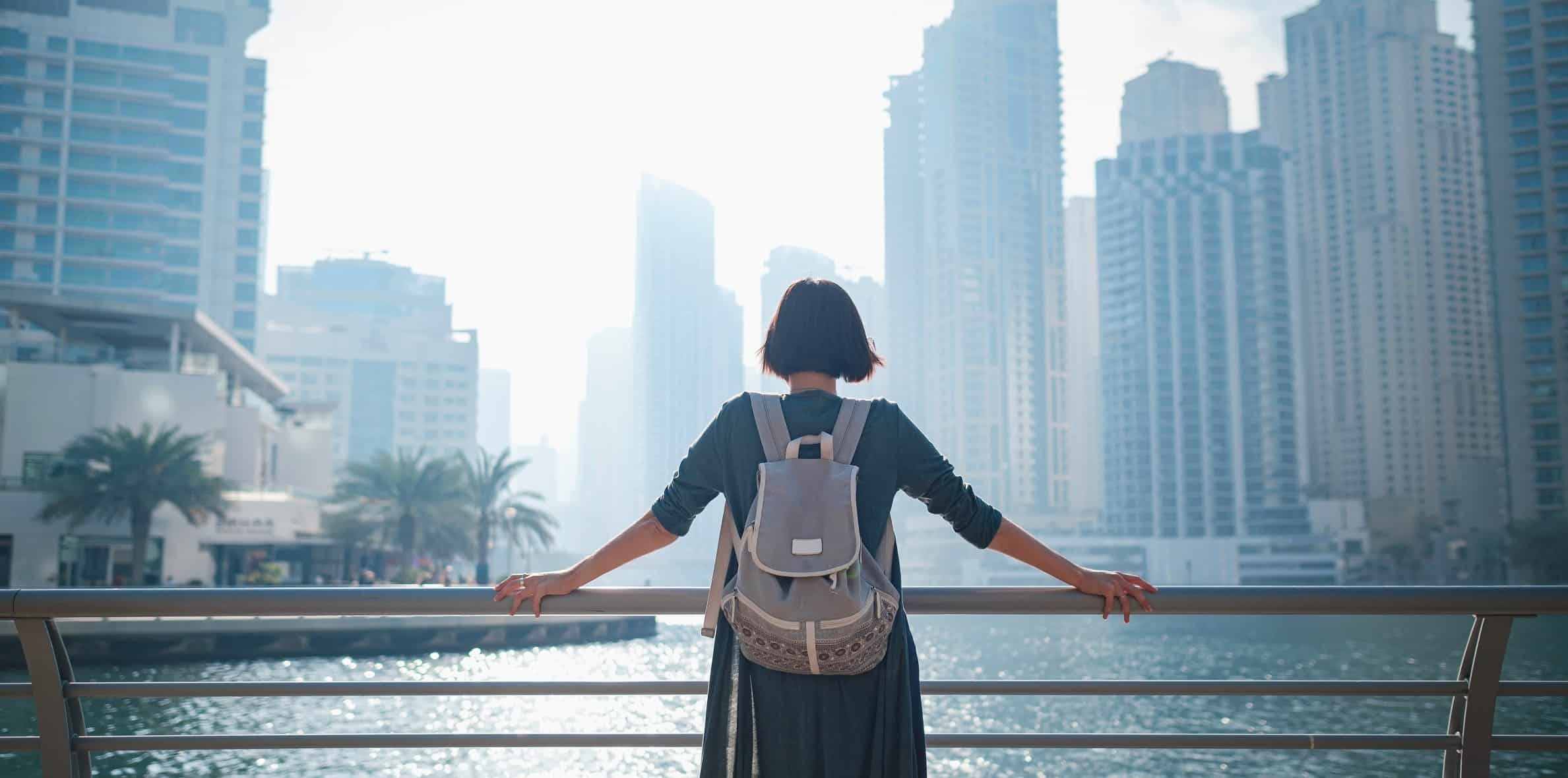 Girl with a backpack holding a railing and looking into the city