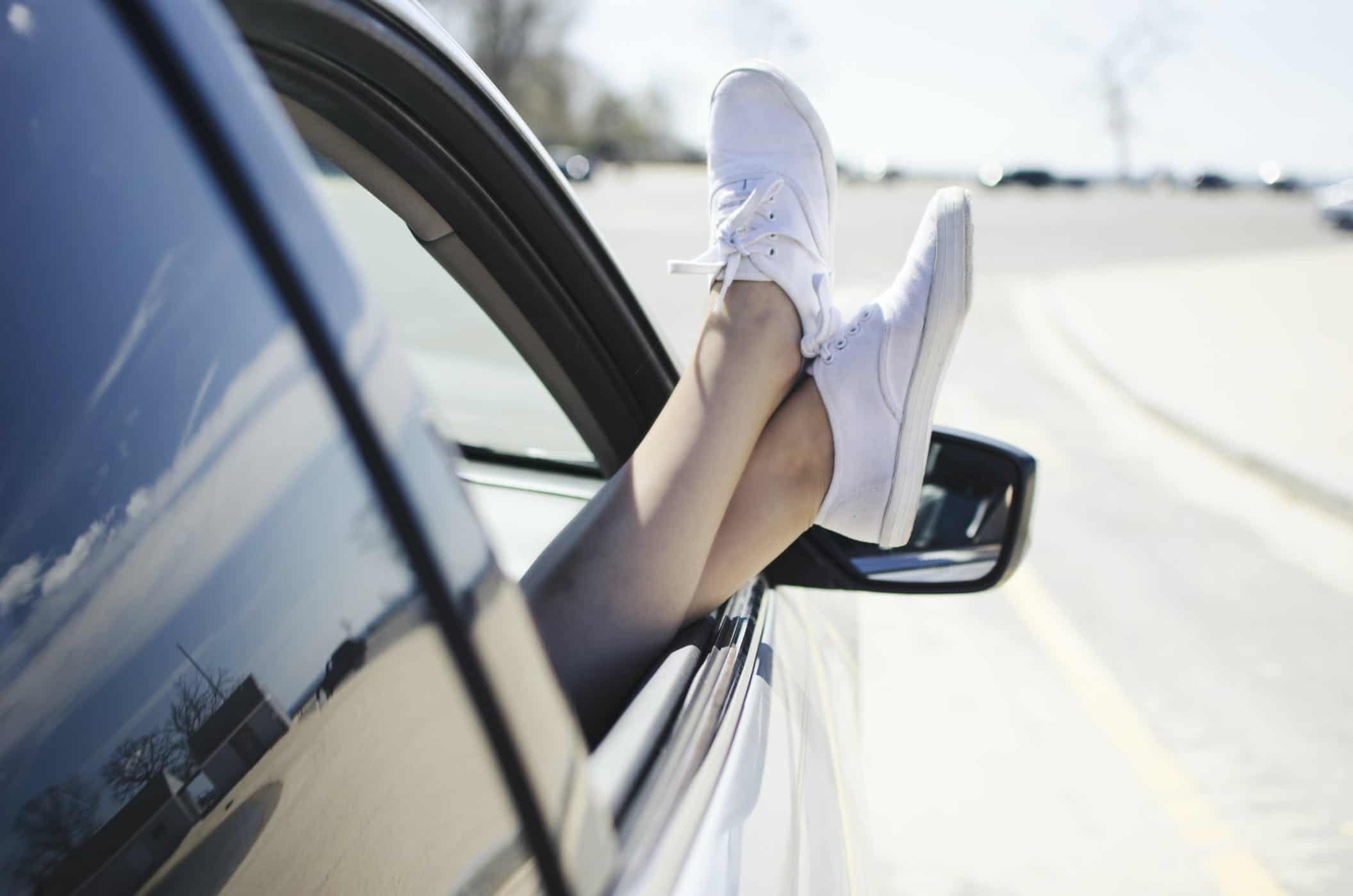 girl in a car on a road trip with her while sneakers hanging out the window