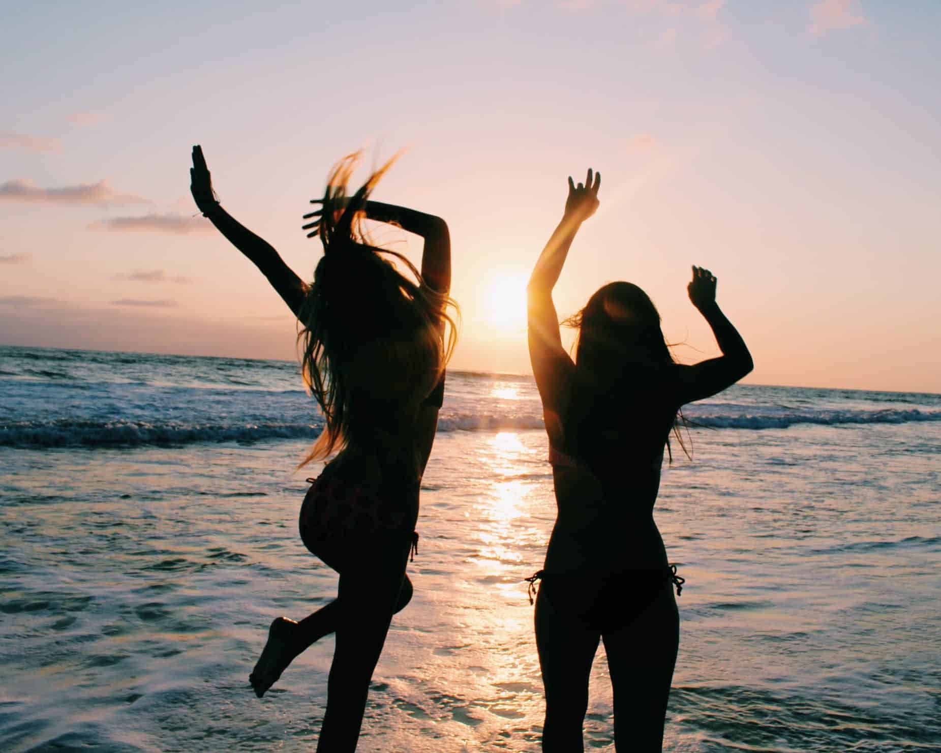 Two girls dancing on the beach at sunset