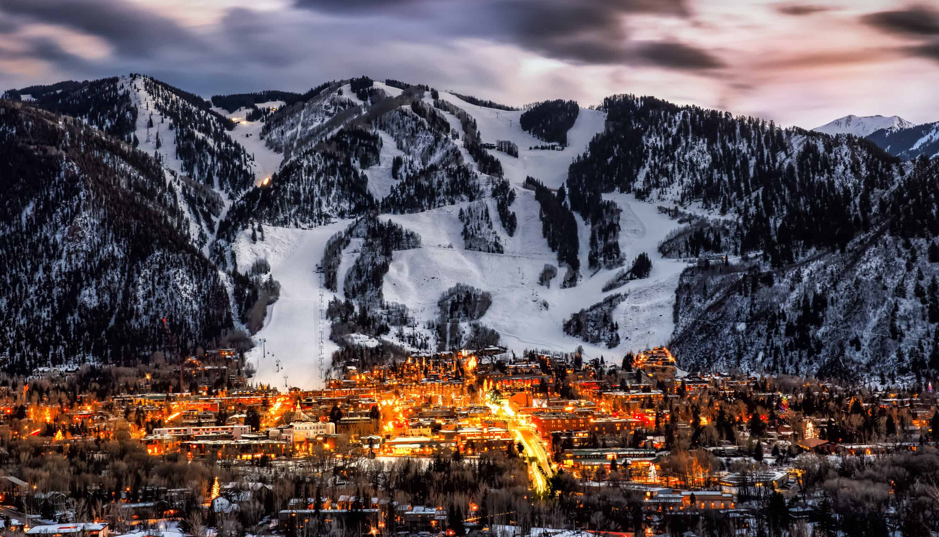 Aspen, CO skyline at sundown with a large mountain in the background and the town below it lit up.