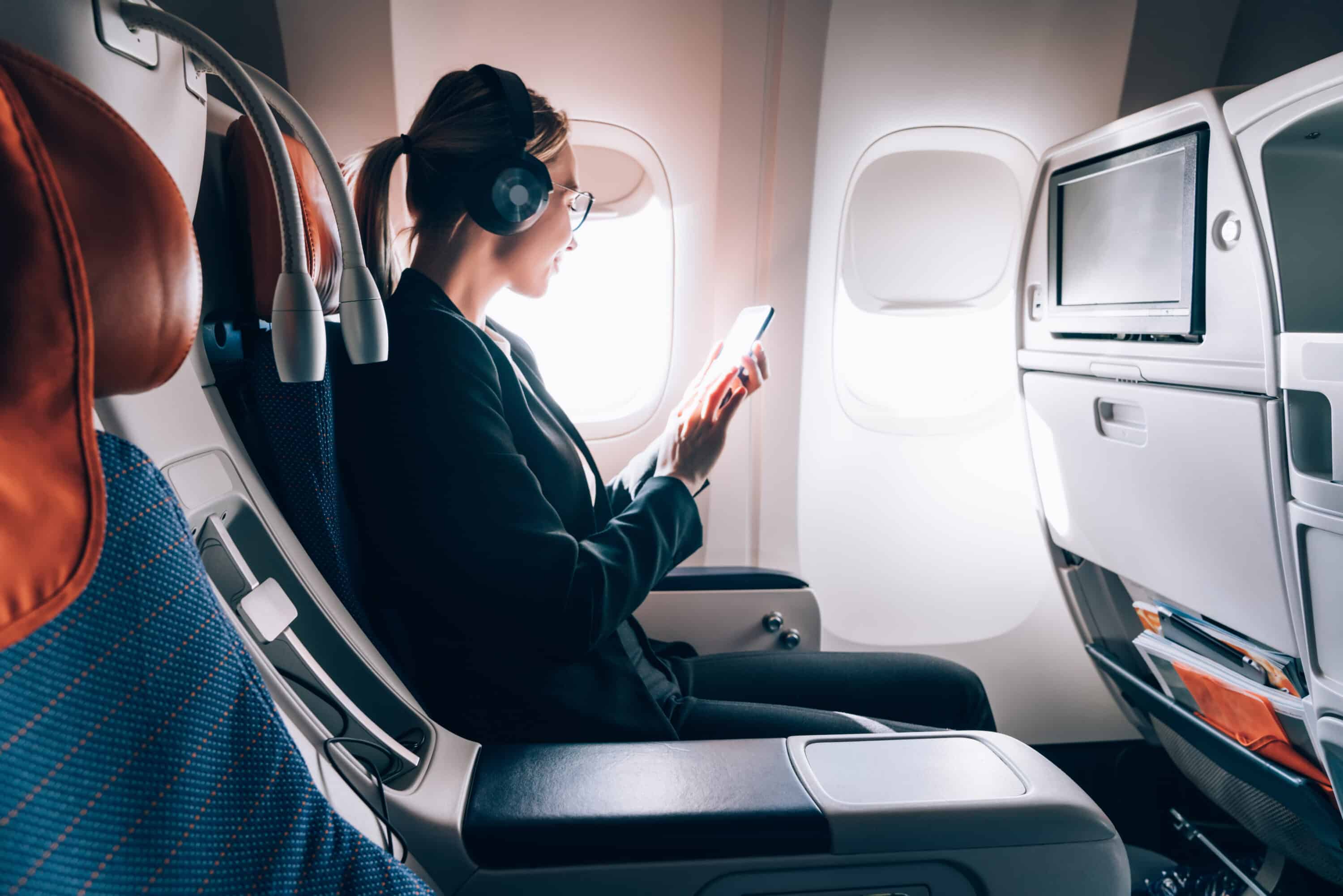 Woman sitting on a plane reading her phone with noise cancelling headphones on.