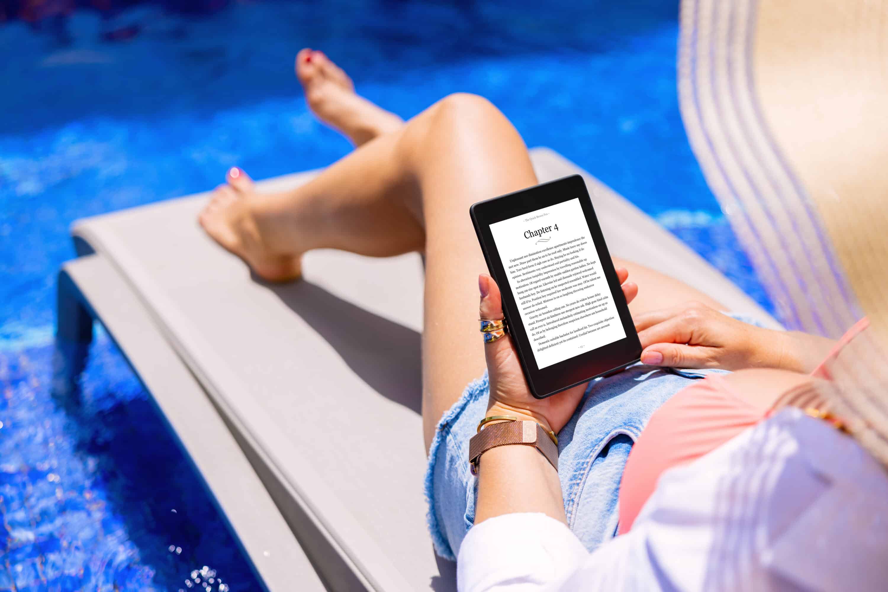 Woman lounging on a lounge chair in a pool reading a book on a Kindle.