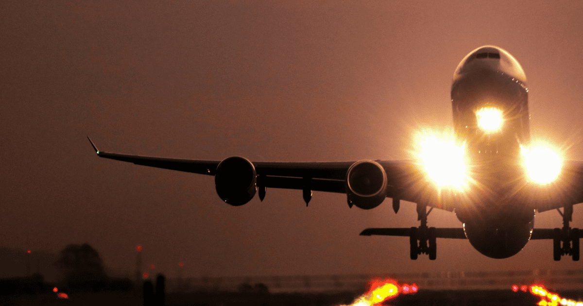 Airplane with lights on taking off from a runway at sundown.
