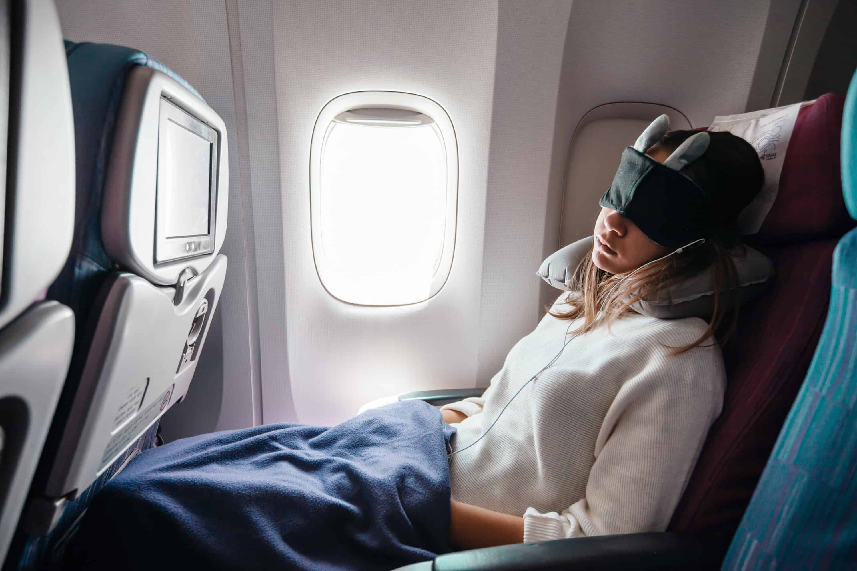 Yound lady sleeping on a plane with an eye mask and neck pillow. 