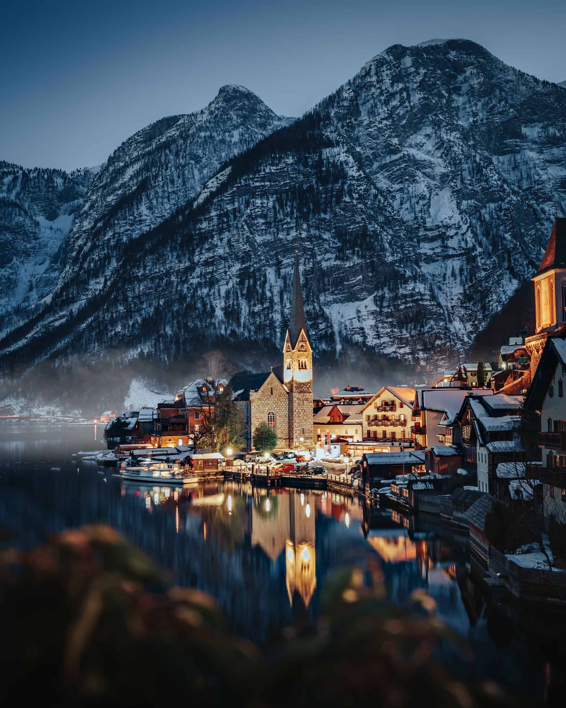 Hallstatt, Austria lit up at night with large snowy mountains in the background. 