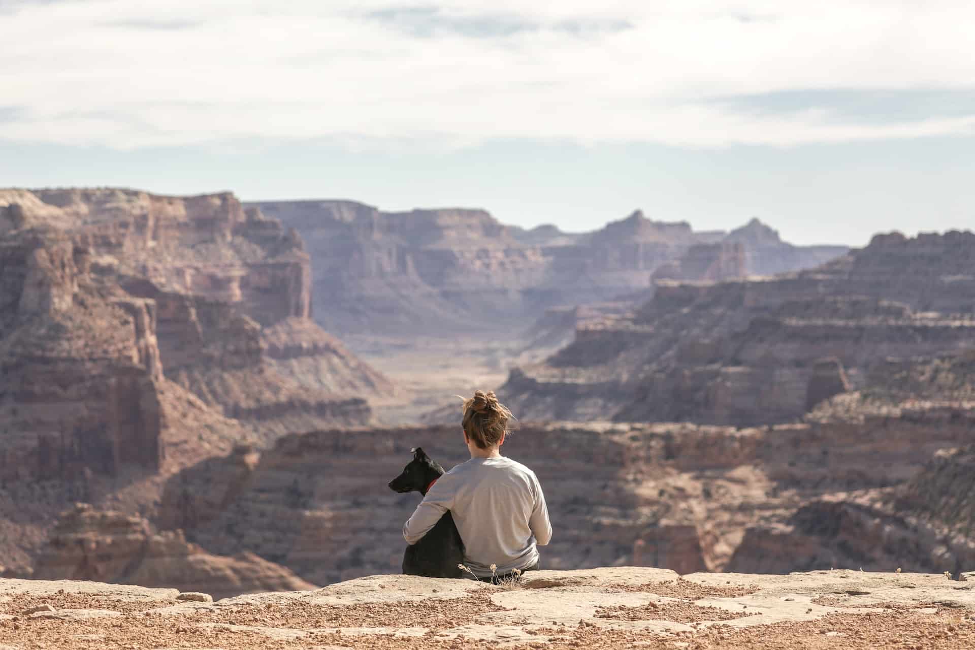 woman-with-dog-sitting-on-grand-canyon-cliff