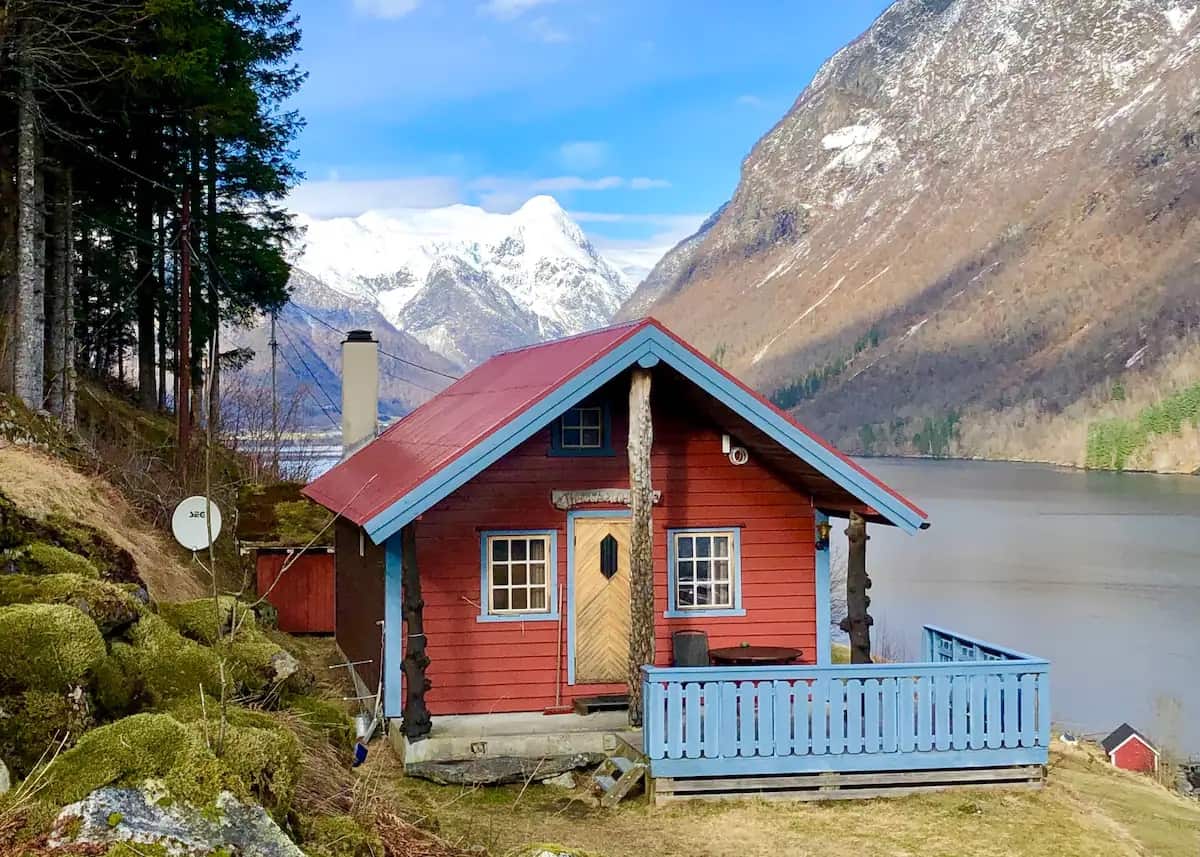 The exterior view of Halvardhytta - Fjærland Cabins in Norway with snow capped mountains in the background and a river below the house. 
