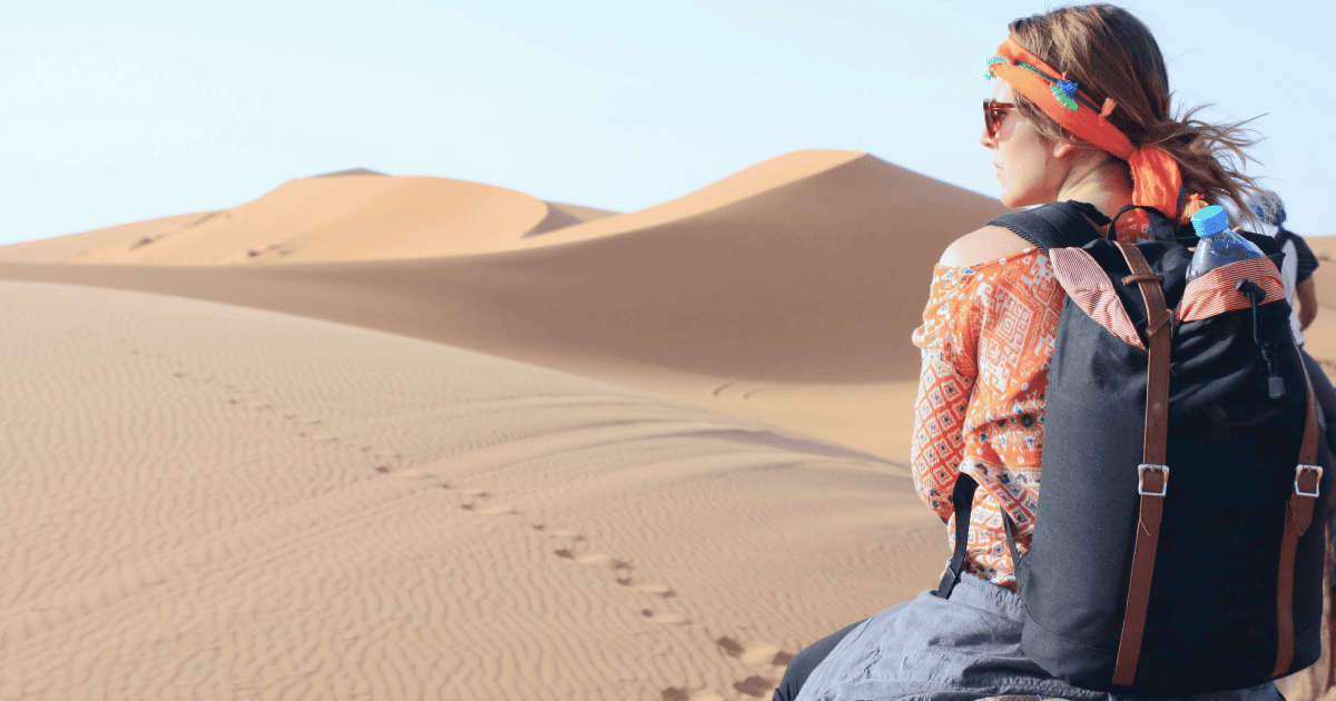 female solo traveler riding a camel through the desert with a backpack on