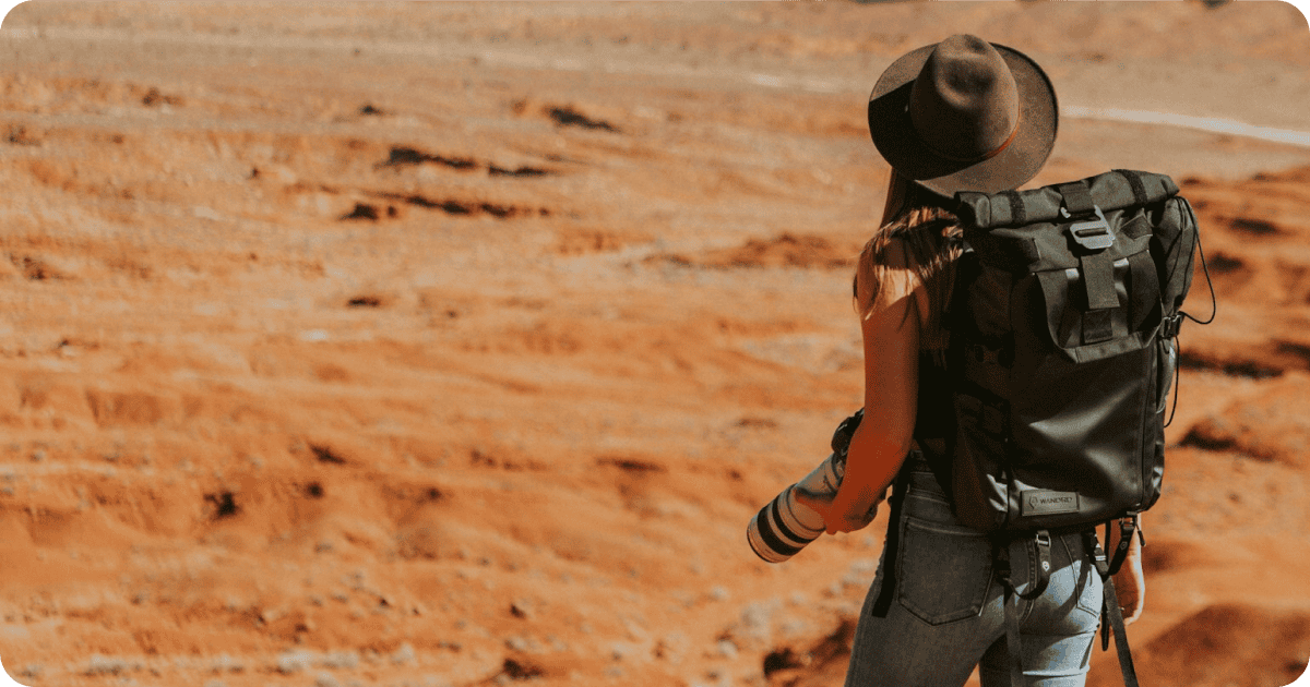 Women with backpack and hat on standing alone in the desert.