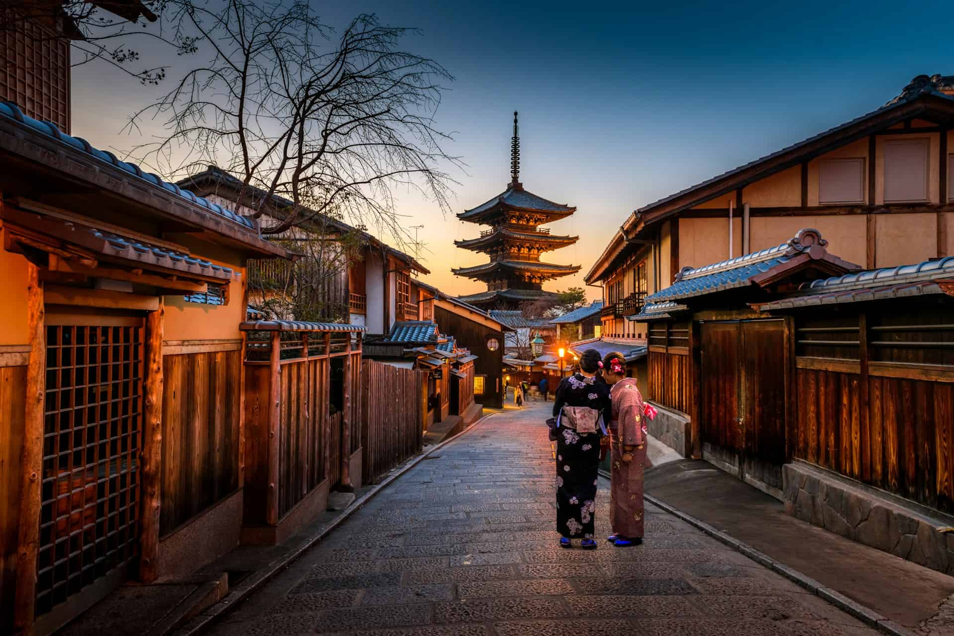 Two women looking down a street at a traditional Japanese building at night. 