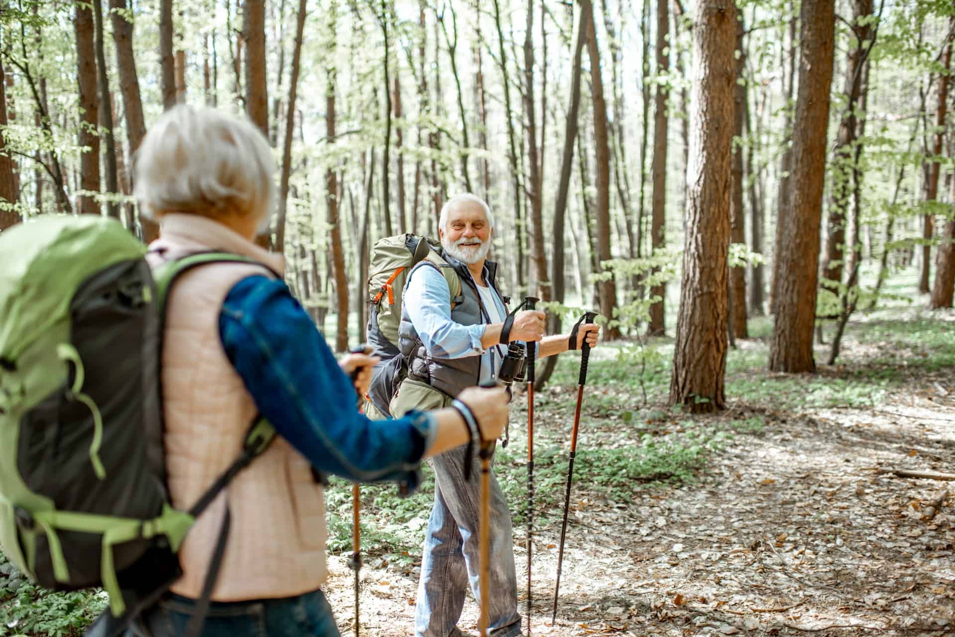 Senior couple hiking with walking sticks and the man has a bright smile while looking at the woman